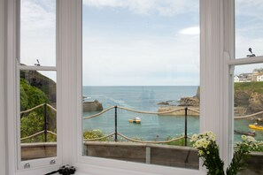 Blick aufs Meer durch ein Fenster mit einer Seilsperre, ein kleines Boot und eine Klippe.