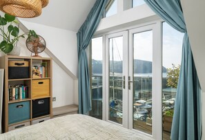 Ein Schlafzimmer mit einem Bett, einem Holzregal, einem Fenster mit Vorhängen und Blick auf Boote draußen.