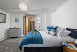 Ein Schlafzimmer mit Bett, Kommode, Nachttisch, Lampe und einem Fenster mit Musterglas.