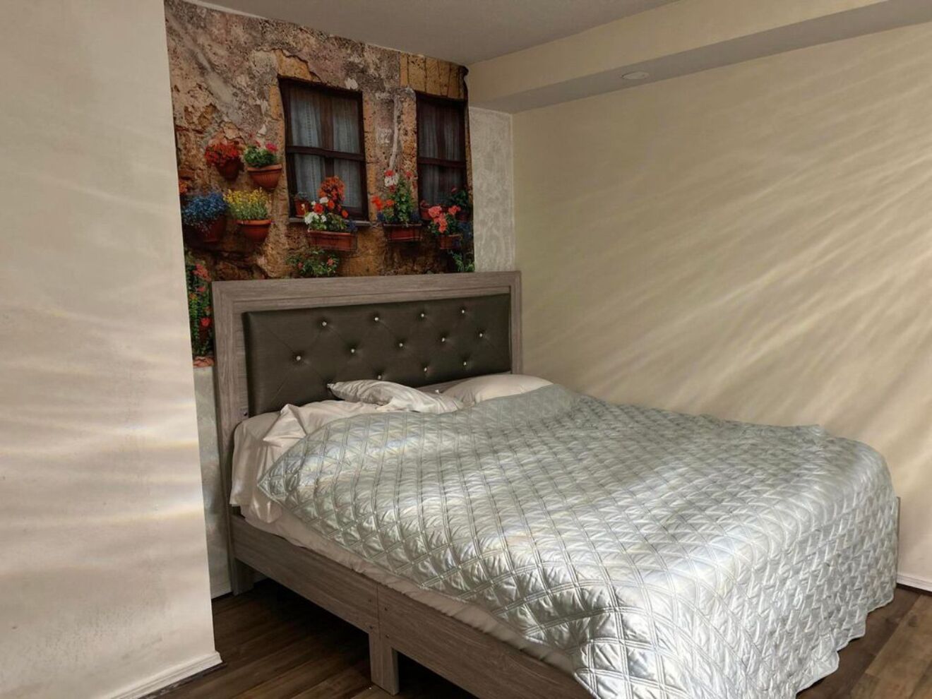 Une chambre à coucher avec un lit, une tête de lit, un mur à surface texturée et une fenêtre avec des rideaux.