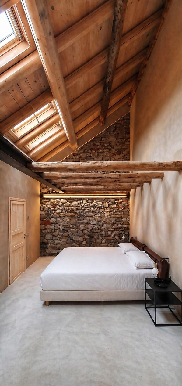 Ein Schlafzimmer mit Steinwand, Holzbalken, einem Bett und einem Oberlicht.