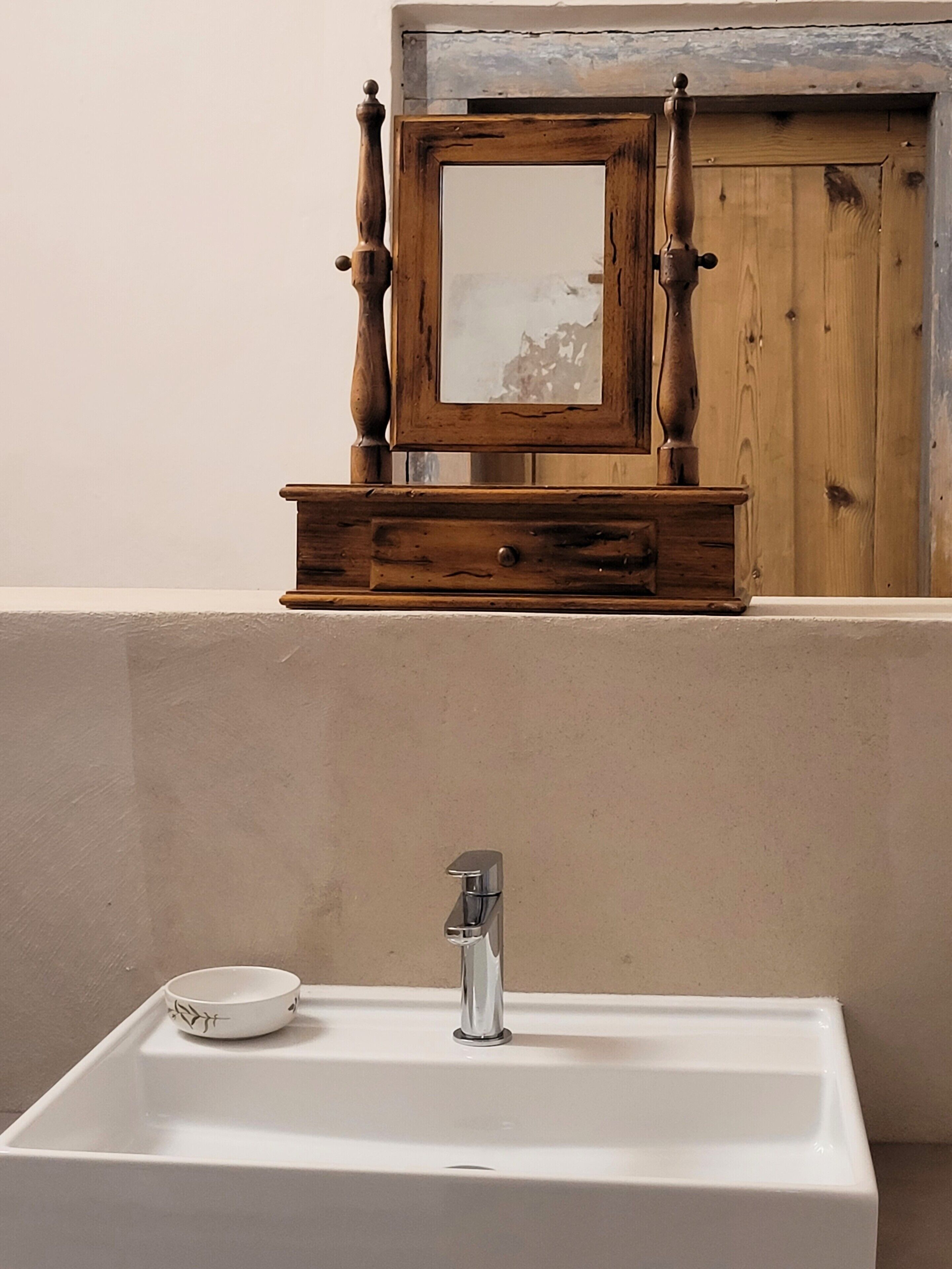 Een badkamer met een wit wastafel, een houten kastje met een spiegel, en een houten deur.