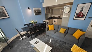 A modern living room with a grey sofa, a coffee table, and a dining area with chairs and a table. - Luxury 4-Bedroom Apartment near Oxford St/ Baker Street (London)