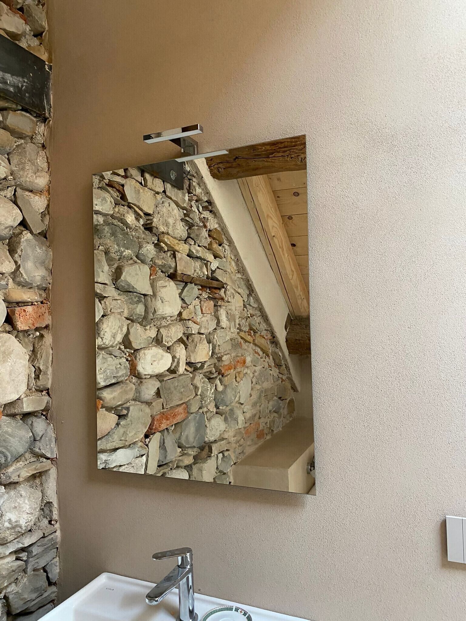 Un baño con pared de piedra, espejo, lavabo y viga de techo de madera.