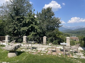 An outdoor seating area with stone tables and chairs, surrounded by a metal fence, with a view of mountains in the background. - 314 - RECORD ROOM (Belluno)