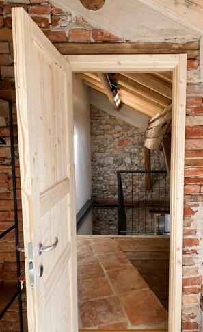 An open wooden door leading to a stone-walled room with a sloped ceiling and a staircase. - 315 - STAIRCASE ROOM (Belluno)