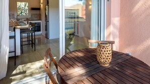 A wooden table with a woven basket, a chair, and a sliding glass door leading to a kitchen and dining area. - Charming Duplex 500m from the port (Hyères)
