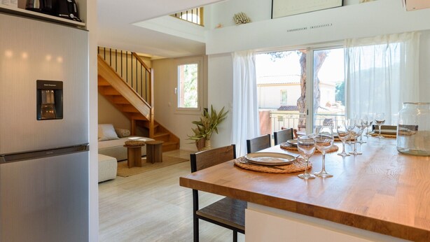 A modern kitchen with a built-in water dispenser, wooden staircase, and a dining area with a wooden table set for a meal. - Charming Duplex 500m from the port (Hyères)