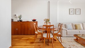 Ett modernt vardagsrum med ett runt matbord i trä, trästolar, en beige soffa och en vit vägg med två inramade tavlor.