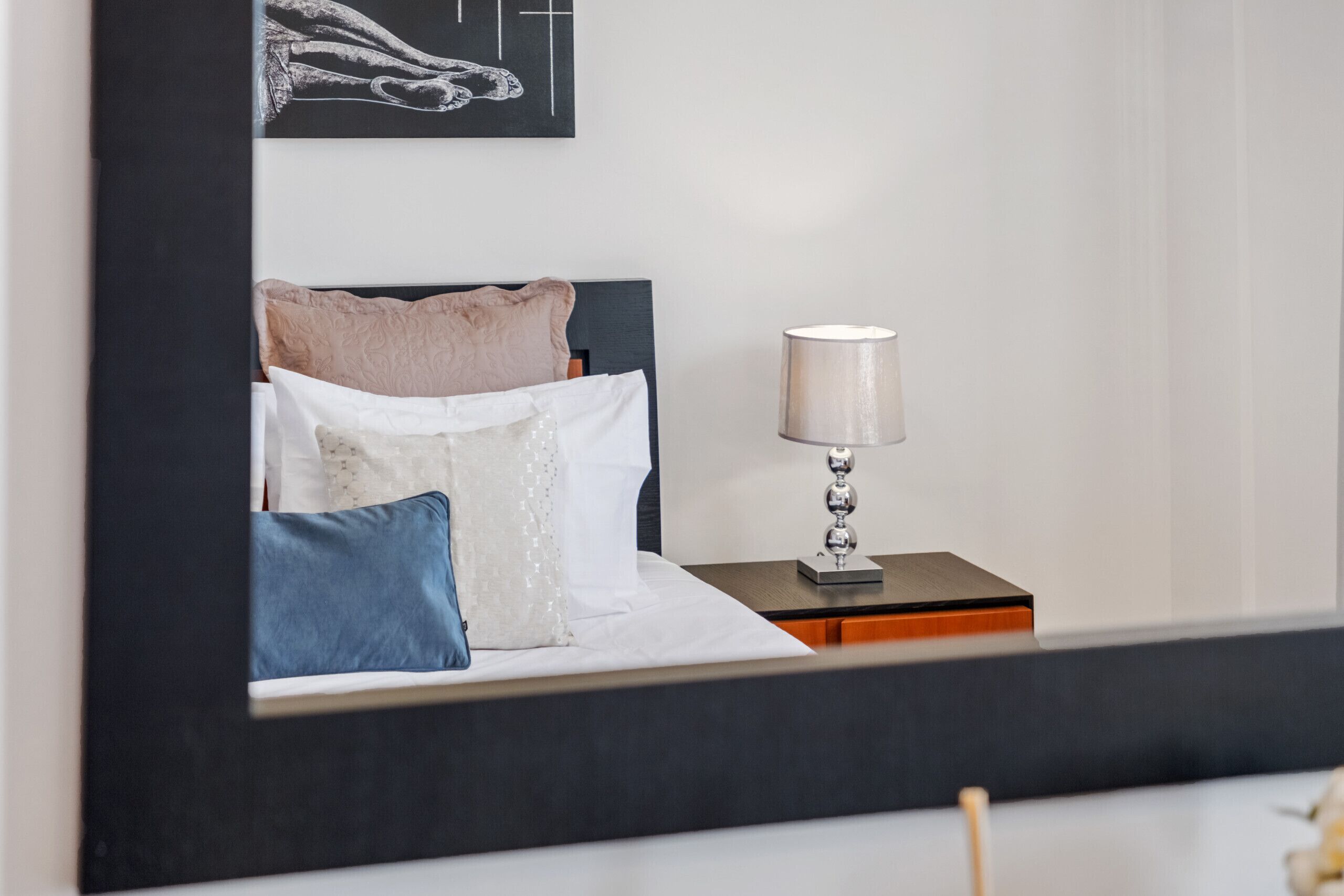 A neatly made bed with pillows, a bedside lamp, and a framed artwork on the wall.