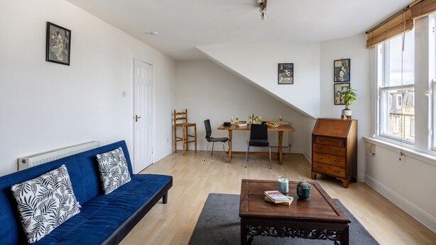 A living room with a blue sofa, a wooden coffee table, a dining table with chairs, and a window with blinds. - Stylish 1BR in Edinburgh New Town (Edinburgh)