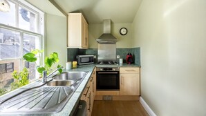 A compact kitchen with a sink, stove, microwave, and cabinets. - Stylish 1BR in Edinburgh New Town (Edinburgh)