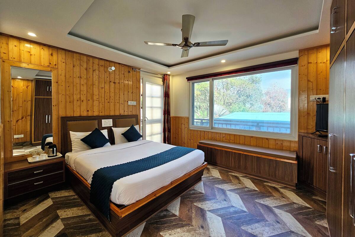 A bedroom with a bed, wooden walls, a ceiling fan, a window with a view, and a television.