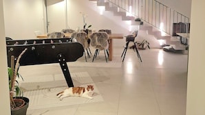 En rummelig opholdsstue med trappe, spisebord med stole og en kat, der ligger på et tæppe.