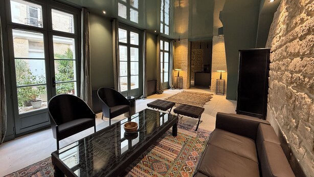 Een moderne woonkamer met een glazen salontafel, zwarte stoelen, een bank en een kamerkleed met een patroon.