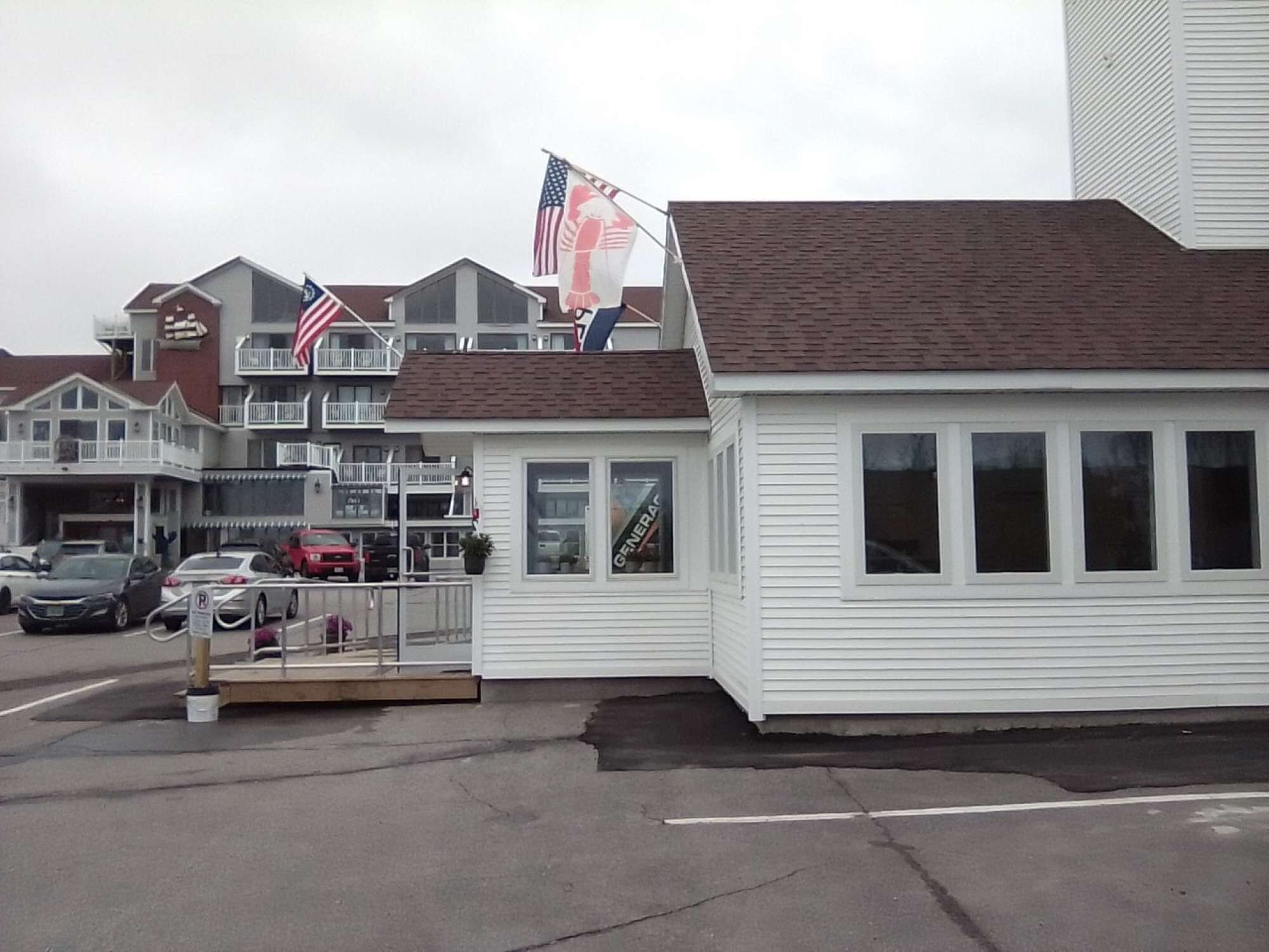 A small white building with a brown roof, a sign reading 'GENERA,' and multiple American flags.