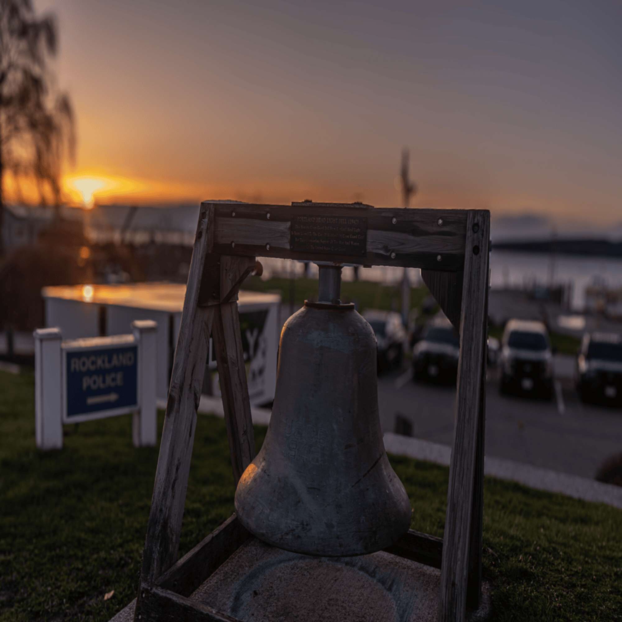 A police siren mounted on a wooden frame with a sign for Rockland Police in the background.