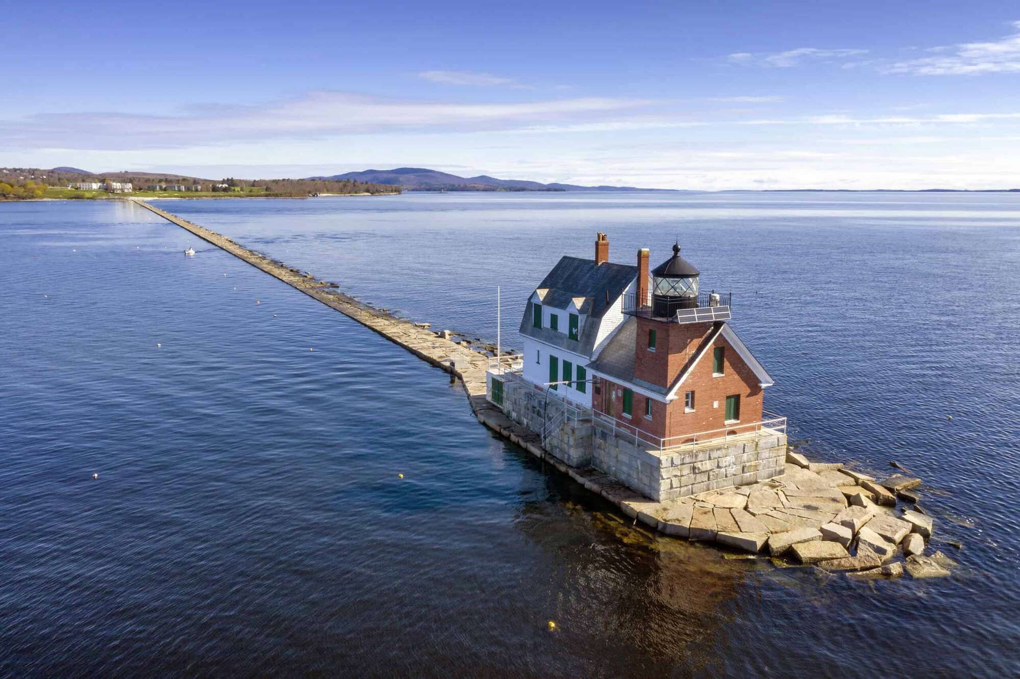 A houseboat with a stone foundation, a chimney, and a balcony on a calm lake.