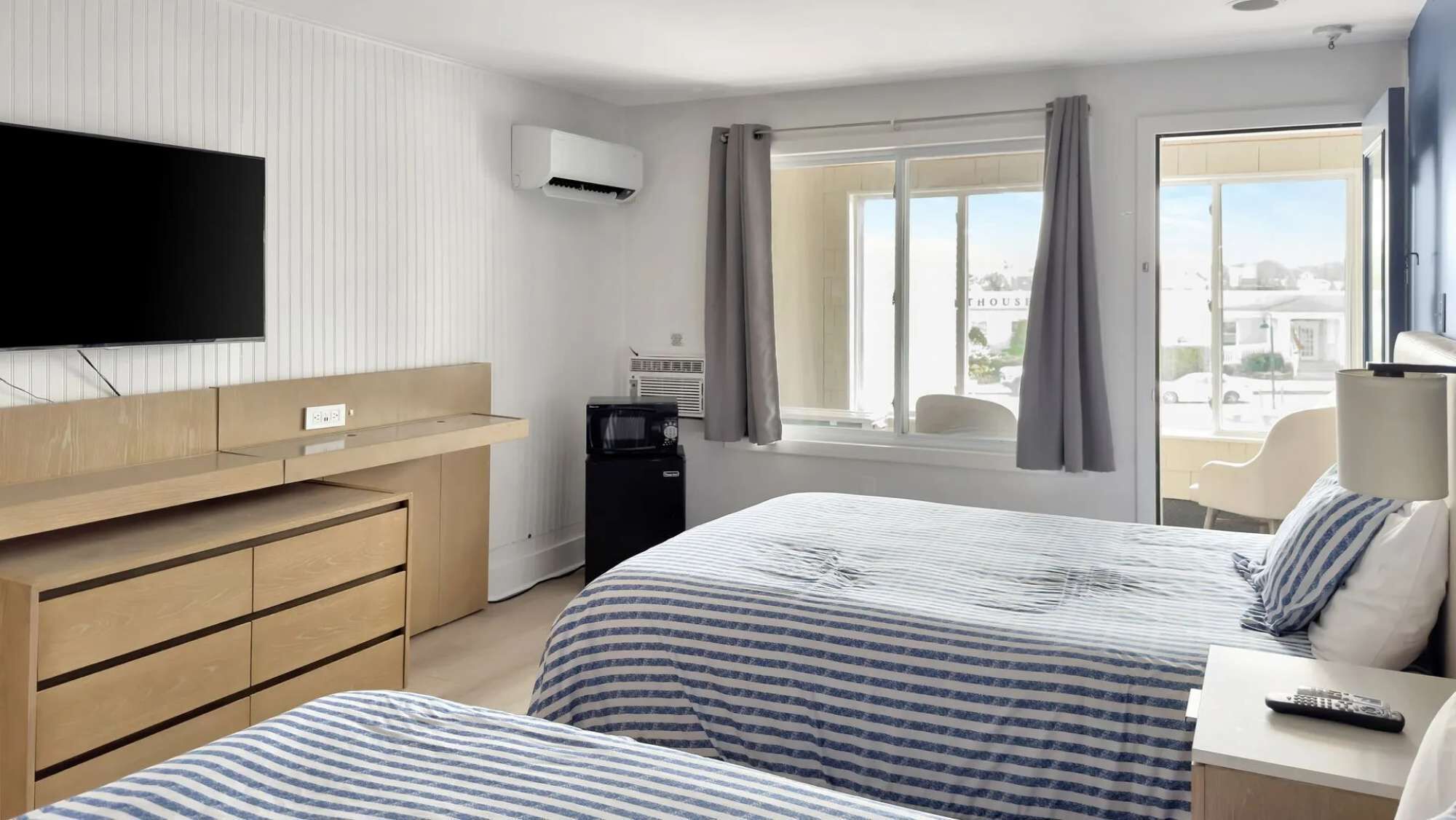 A hotel room with two beds, a TV, a desk, a chair, a window with curtains, and a view of the city.