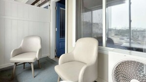 Ein Zimmer mit zwei weißen Sesseln, einer blauen Tür und einem Fenster mit Blick auf die Stadt.