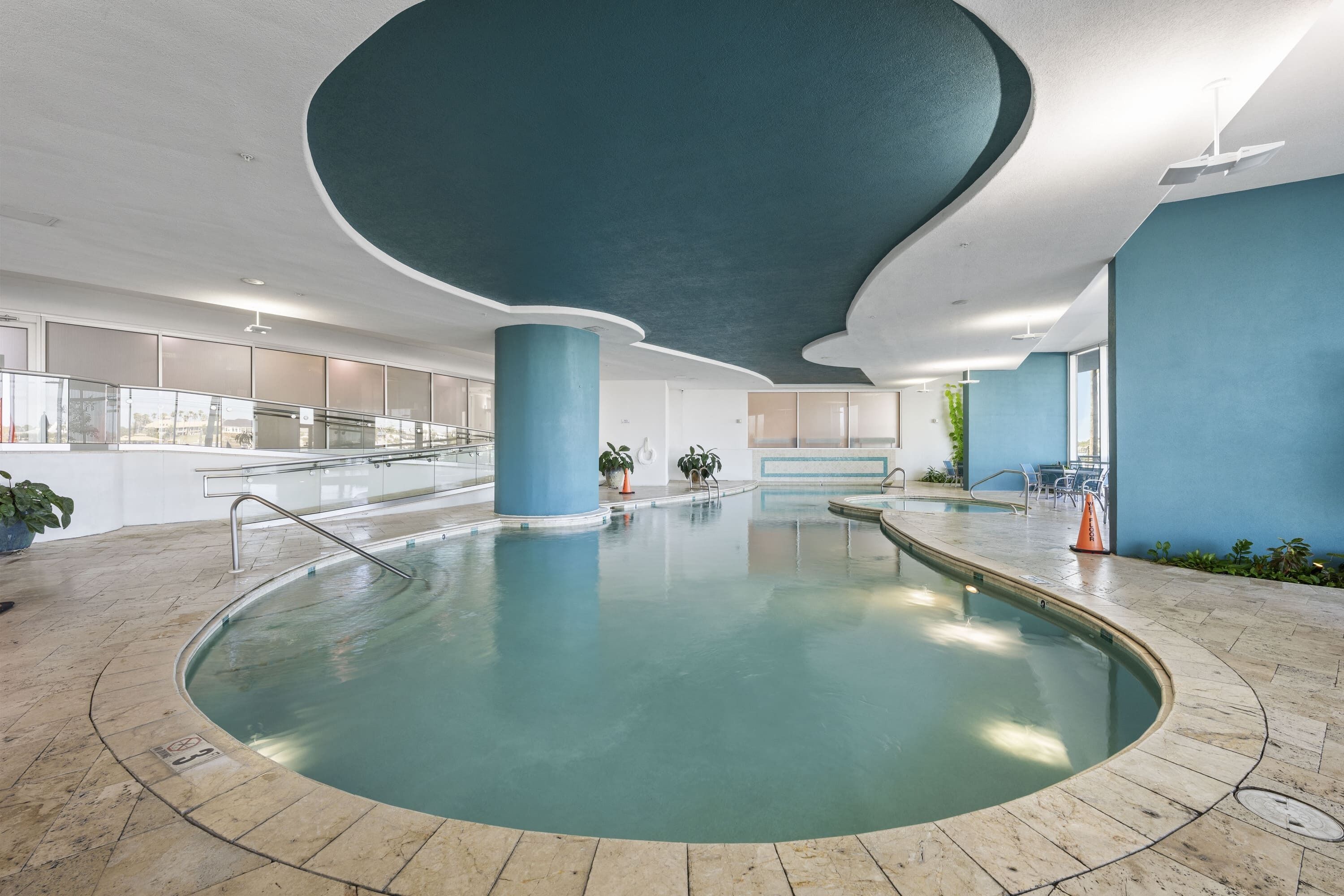 An indoor swimming pool with a curved ceiling, clear glass railings, and potted plants.
