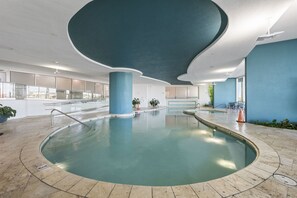 Ein Innenpool mit gewölbter Decke, transparenten Glasgeländern und Kübelpflanzen.