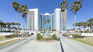 Een modern hotel met een gebogen gevel, palmbomen en een centraal geplaatst standbeeld.