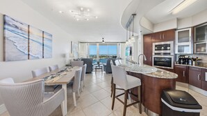 Een moderne keuken met een centraal eiland, een eetgedeelte met stoelen en uitzicht op de oceaan.