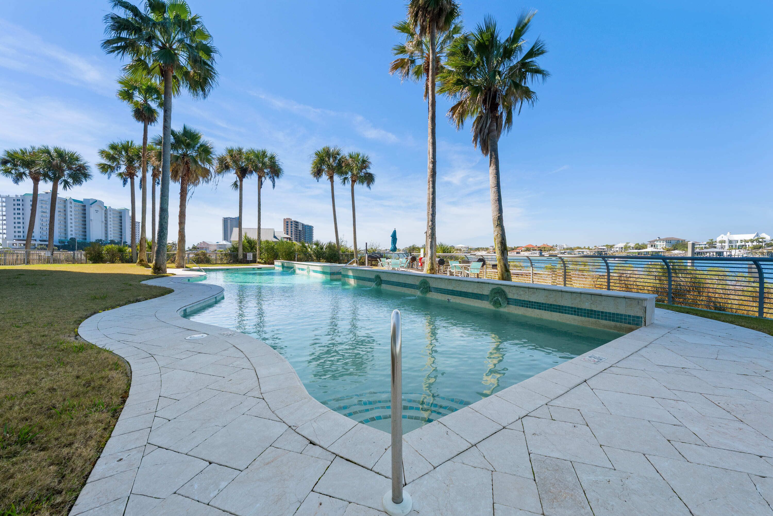 A swimming pool with a curved edge, surrounded by palm trees and a paved walkway.
