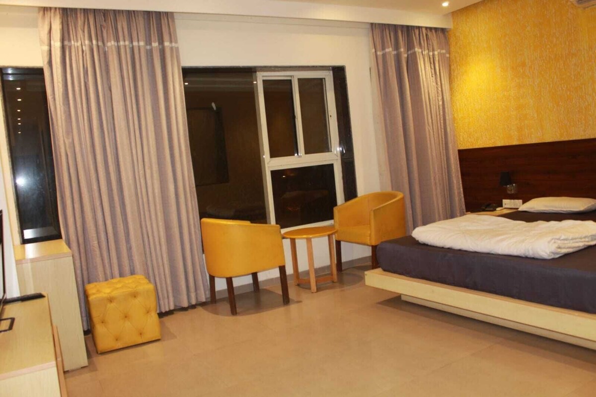 A hotel room with a bed, a desk, two chairs, a small table, and a window with curtains.
