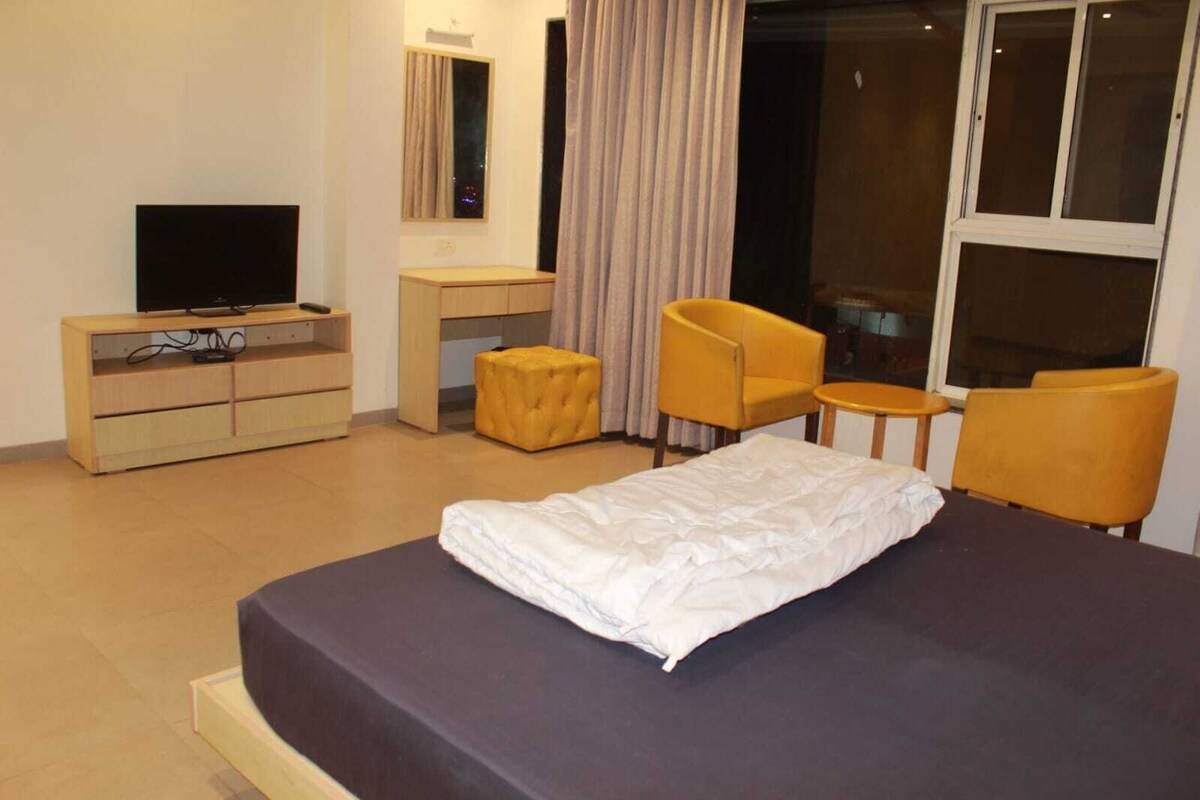 A hotel room with a bed, a desk, a chair, a television, and a window.