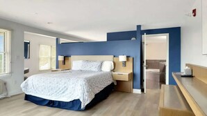 A modern hotel room with a large bed, bedside tables, a desk, and a bathroom visible through an open door. - King + Sofa w/ Balcony + Free Breakfast & Parking (Rockland)