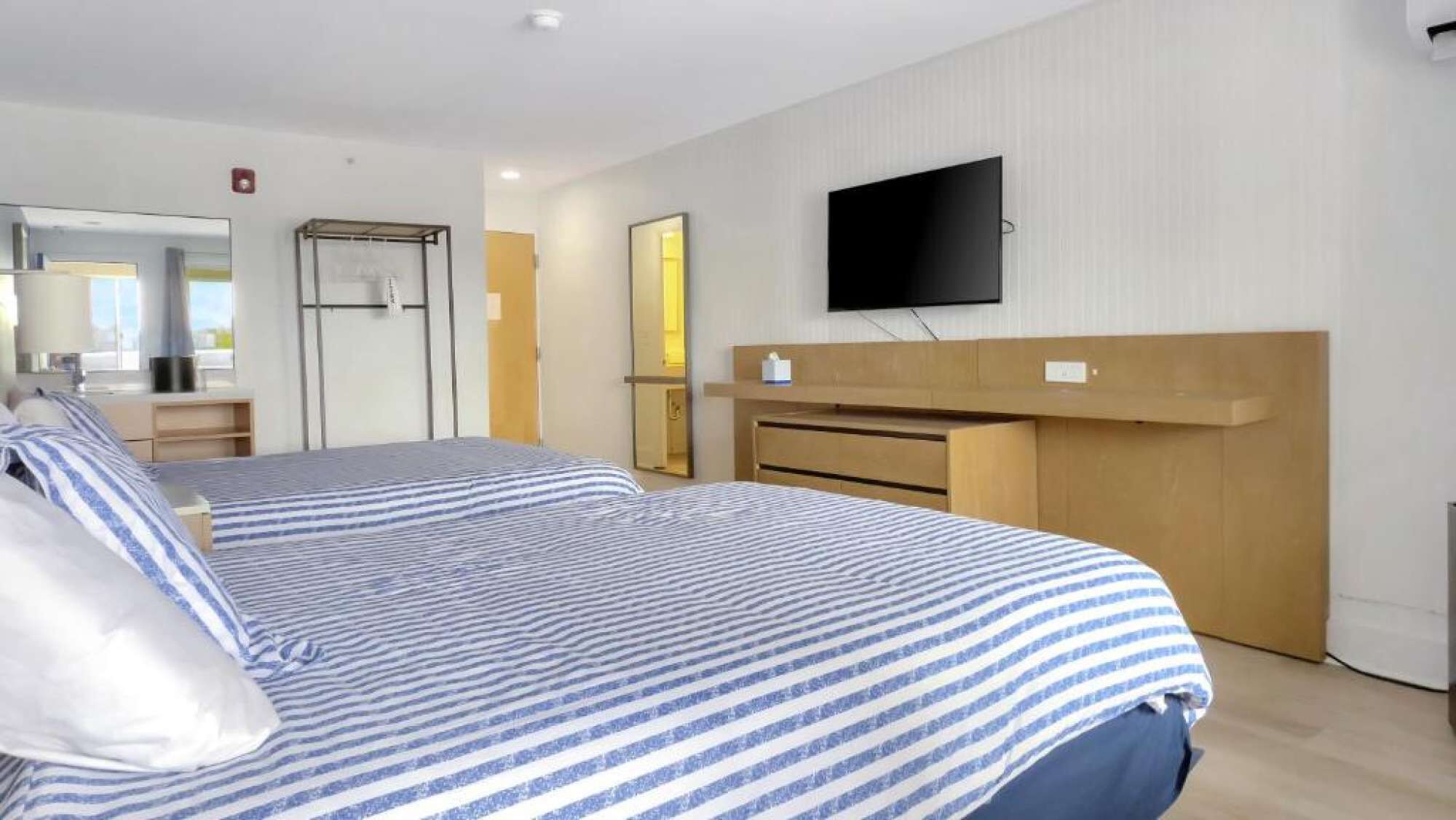 A hotel room with two beds, a flat-screen TV mounted on the wall, a wooden headboard, and a mirror.
