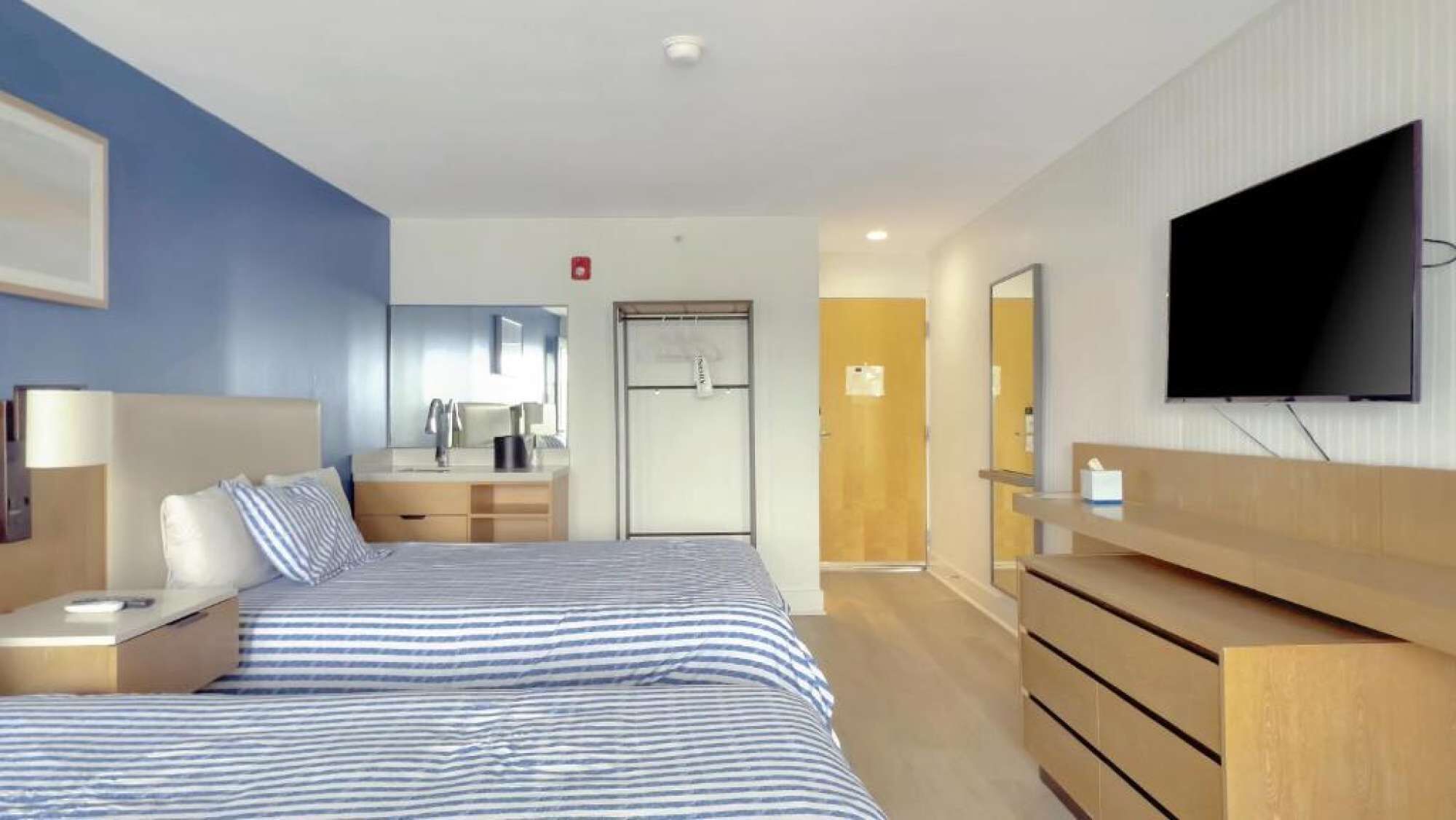 Ein Hotelzimmer mit Bett, Nachttischen, Fernseher, Spiegel, Kleiderschrank und einer Tür zu einem Badezimmer.