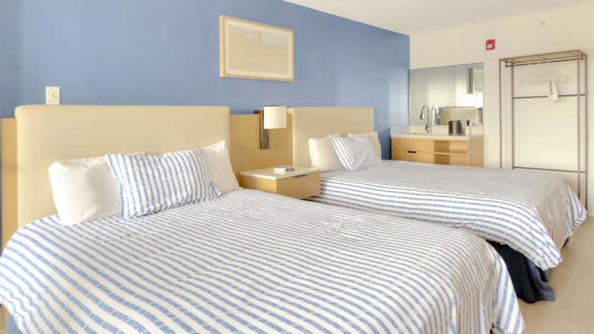 A hotel room with two beds, a nightstand, a lamp, a dresser, and a mirror.