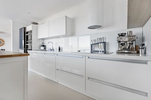 Eine moderne Küche mit weißen Schränken, einem eingebauten Ofen, einer Kaffeemaschine und einem Messerblock.