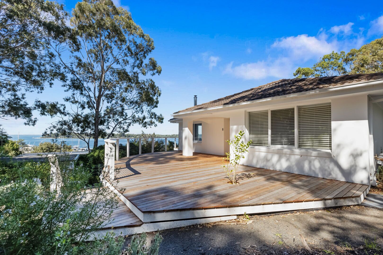 A house with a wooden deck, a white exterior, and a view of the sea.