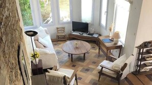 Ein großzügiger Wohnbereich mit einem großen Fenster, einem Fernseher und einem runden Holztisch.
