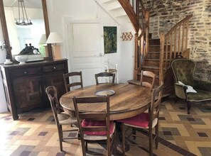 A dining area with a wooden table, chairs, a chandelier, a staircase, and a stone wall. - Seaside family home with terrace and garden 🌸 (Saint-Gilles-Croix-de-Vie)
