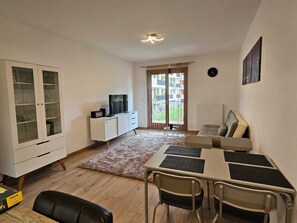 A living room with a TV, a cabinet, a sofa, a dining table with chairs, and a window with curtains.