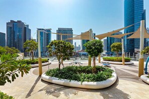 A modern urban plaza with geometric landscaping, including planters and trees, surrounded by high-rise buildings. - Imperial Avenue Downtown by UniDwellers (Dubai)