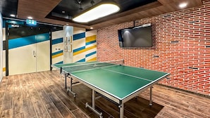 Une table de ping-pong dans une pièce avec un mur en briques, un téléviseur fixé au mur et un plafond doté d’un éclairage encastré.