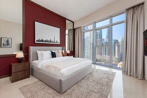 Een moderne hotelkamer met een groot bed, uitzicht op de stad, een lijst met foto aan de muur en een nachtkastje met lamp.