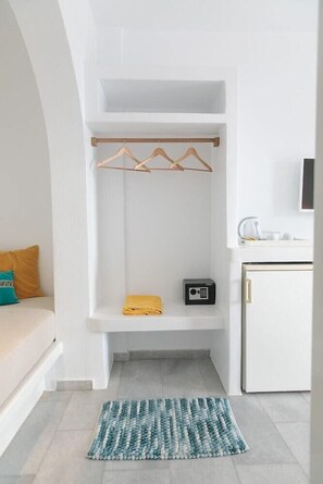 Une chambre compacte dotée d’un placard intégré, d’un petit coin salon avec un coussin, d’un four à micro-ondes et d’un téléviseur fixé au mur.