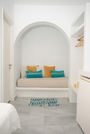 Une pièce avec une alcôve en arc de cercle peinte en blanc, un canapé agrémenté de coussins à motifs, un petit tapis et une armoire blanche.