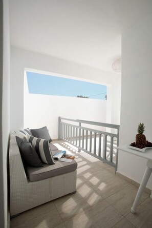 Un balcon avec une balustrade blanche, un canapé gris avec des coussins à rayures et un ananas posé sur une petite table.