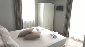 Un lit bien fait, avec des oreillers et des serviettes enroulées, une armoire blanche et un téléviseur fixé au mur.