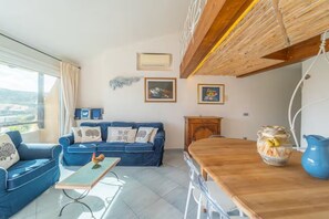 Ein Wohnzimmer mit einem blauen Sofa, einem Holzesstisch und Blick durch ein großes Fenster.