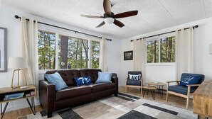 Ein Wohnzimmer mit braunem Sofa, einem Holztisch, einem kleinen Beistelltisch und einem Deckenventilator.