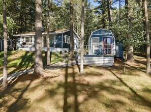 Una cabana amb un porxo i un cobert separat, envoltada d'arbres.